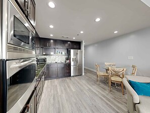 A modern kitchen with dark cabinets, stainless steel appliances, and a dining area with wooden chairs and a table. - Splash by Resort Collection (Panama City Beach)