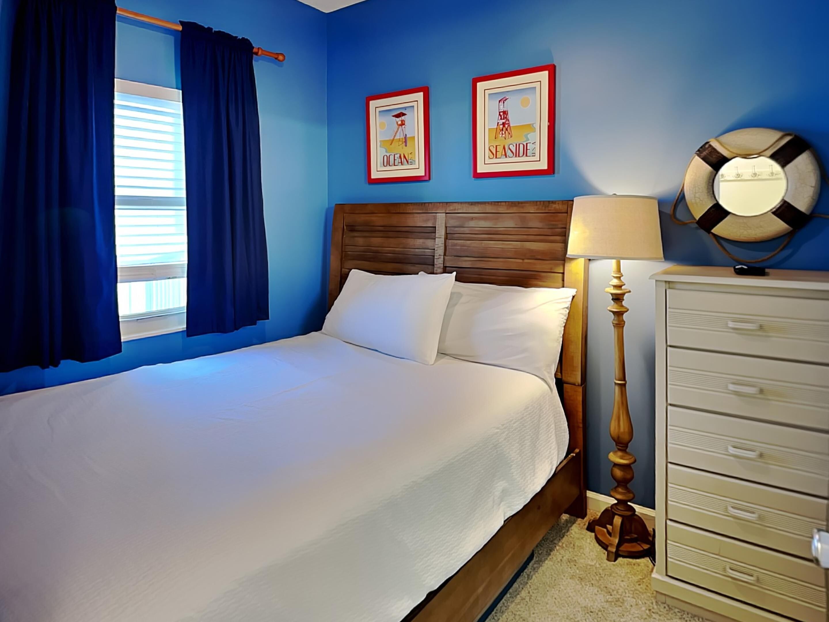 Une chambre à coucher avec une tête de lit en bois, une literie blanche, une table de chevet en bois avec une lampe, et deux tableaux encadrés accrochés au mur.