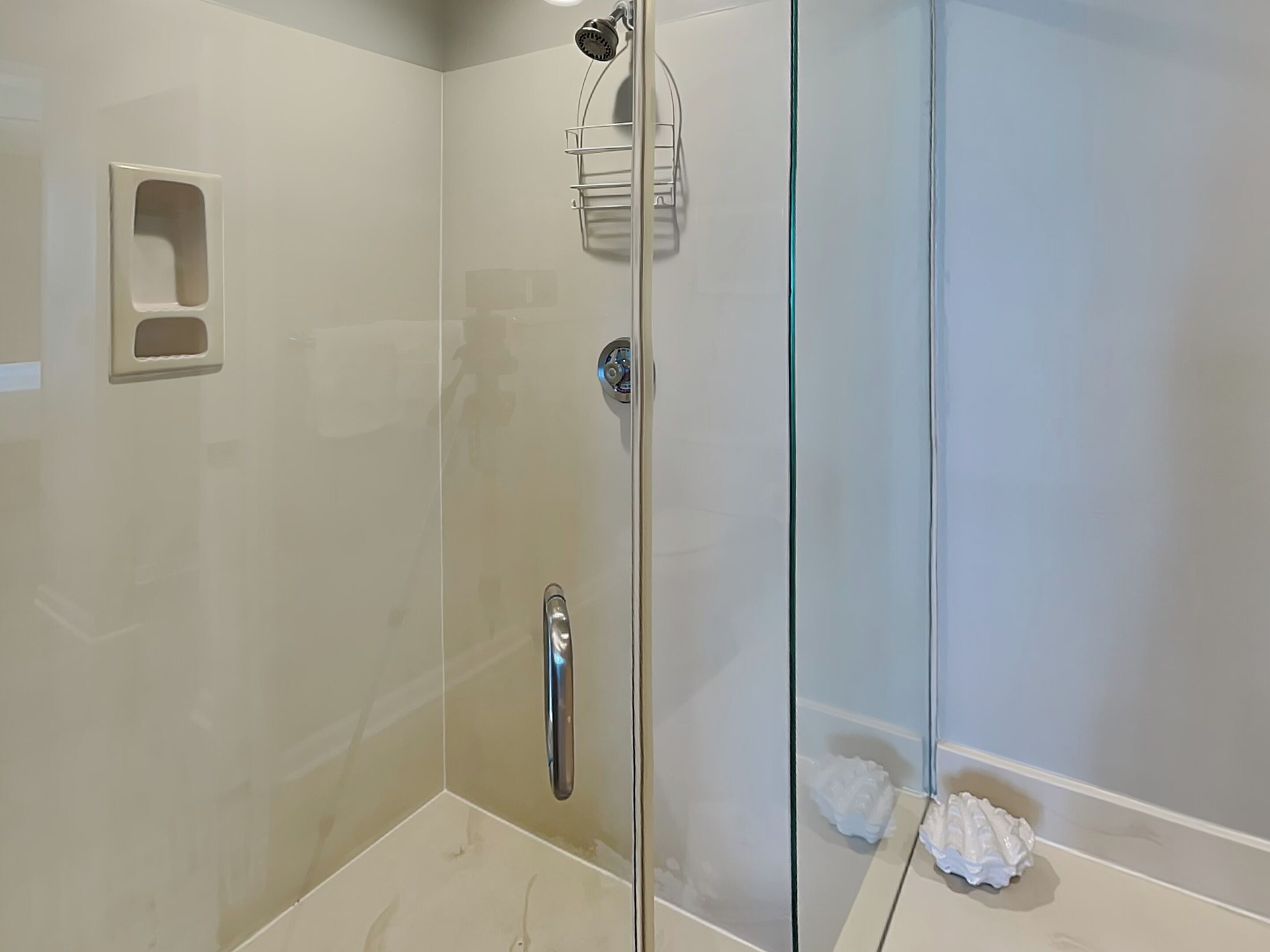 A glass-enclosed shower with a handheld showerhead, a wall-mounted towel rack, and a small shelf.