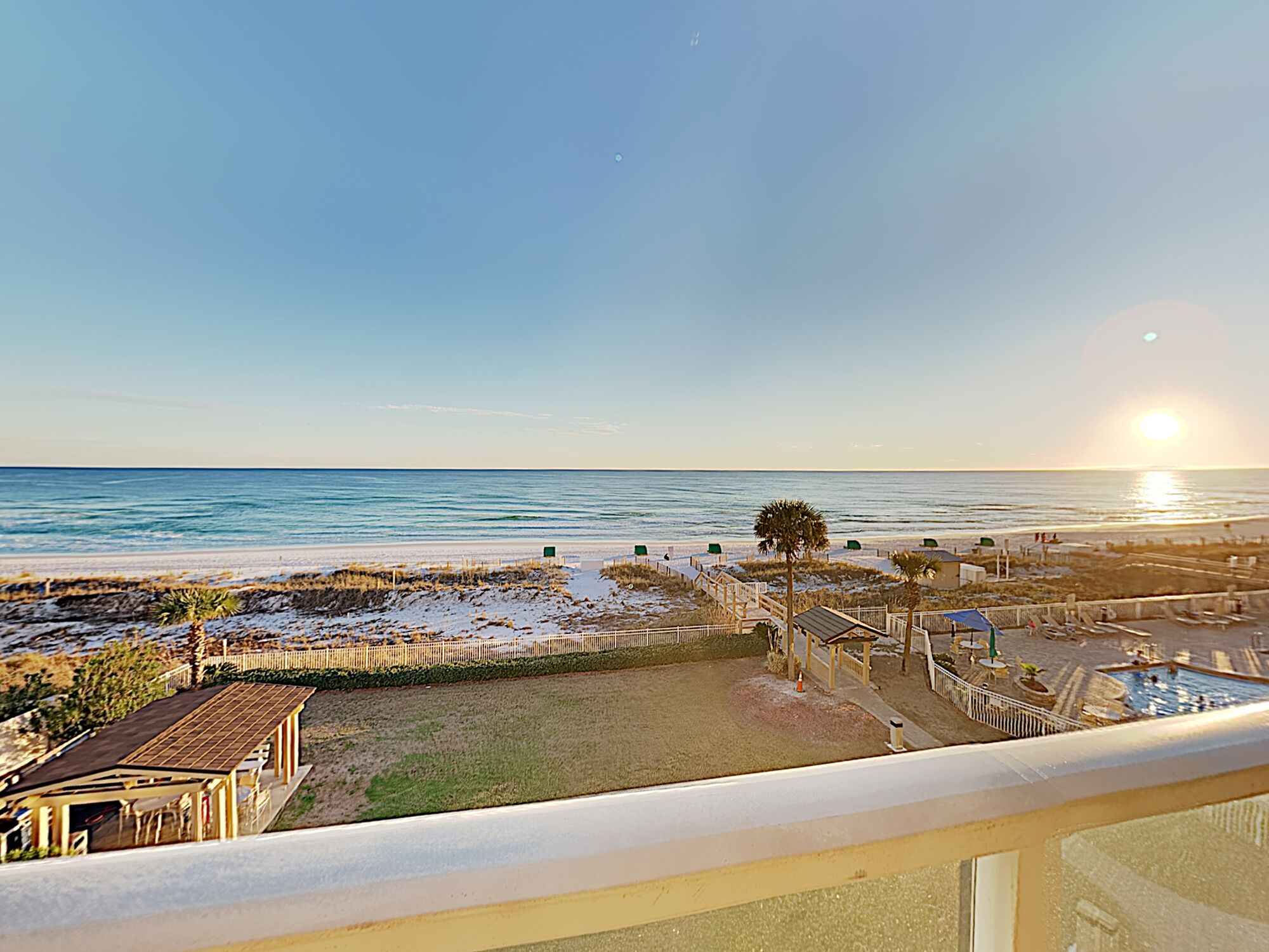 Une vue sur la plage avec une terrasse en bois, un petit bâtiment et un espace clôturé avec des chaises de plage.