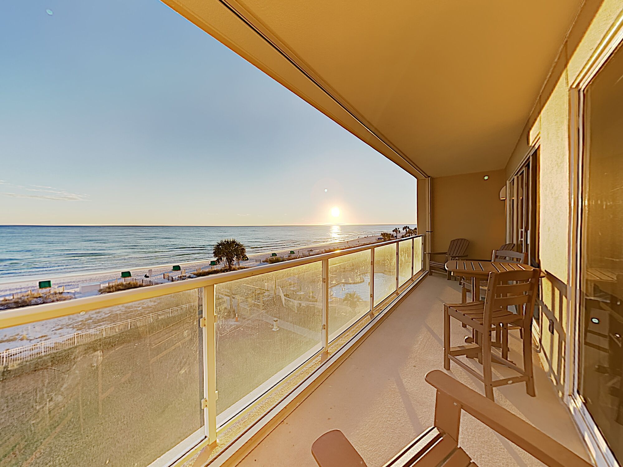 A balcony with a view of the beach and ocean, featuring a table and chairs.