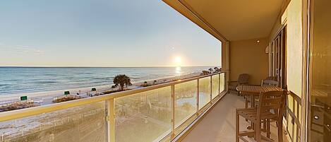 A balcony with a view of the beach and ocean, featuring a table and chairs.