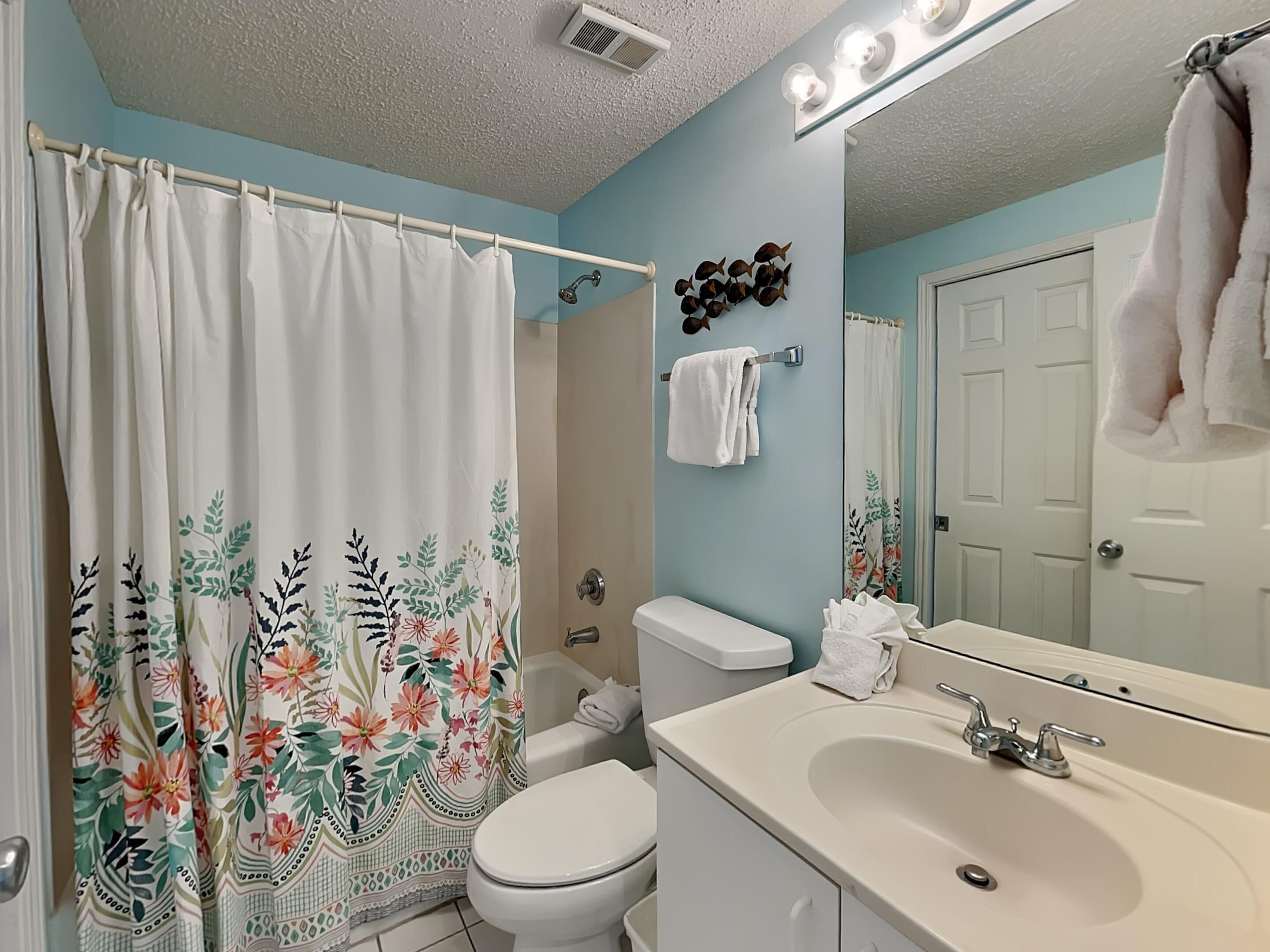 Une salle de bain avec un rideau de douche à motifs floraux, des toilettes, un lavabo avec un miroir et un porte-serviettes.