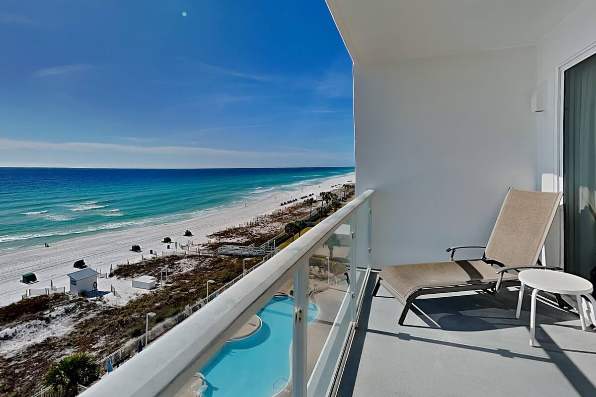 A balcony with a pool, overlooking a beach with a clear view of the ocean and a sandy shoreline.