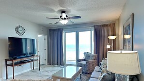 A hotel room with a flat-screen TV, a ceiling fan, a sofa, a chair, a coffee table, and a view of the ocean. - Sterling Sands by Southern Vacation Rentals (Destin)