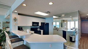 A modern kitchen with white cabinets, a black refrigerator, and a large island with bar stools. - Sterling Sands by Southern Vacation Rentals (Destin)