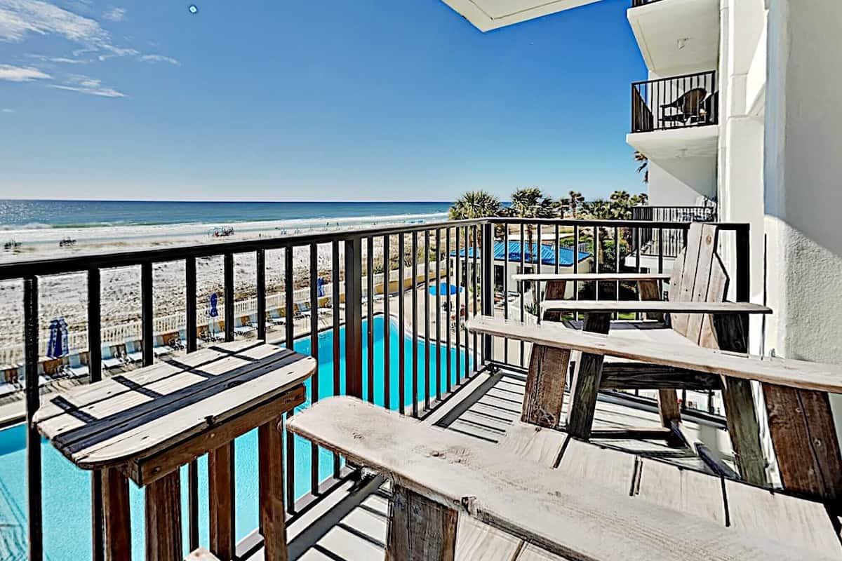 A balcony with a view of the beach and a pool.