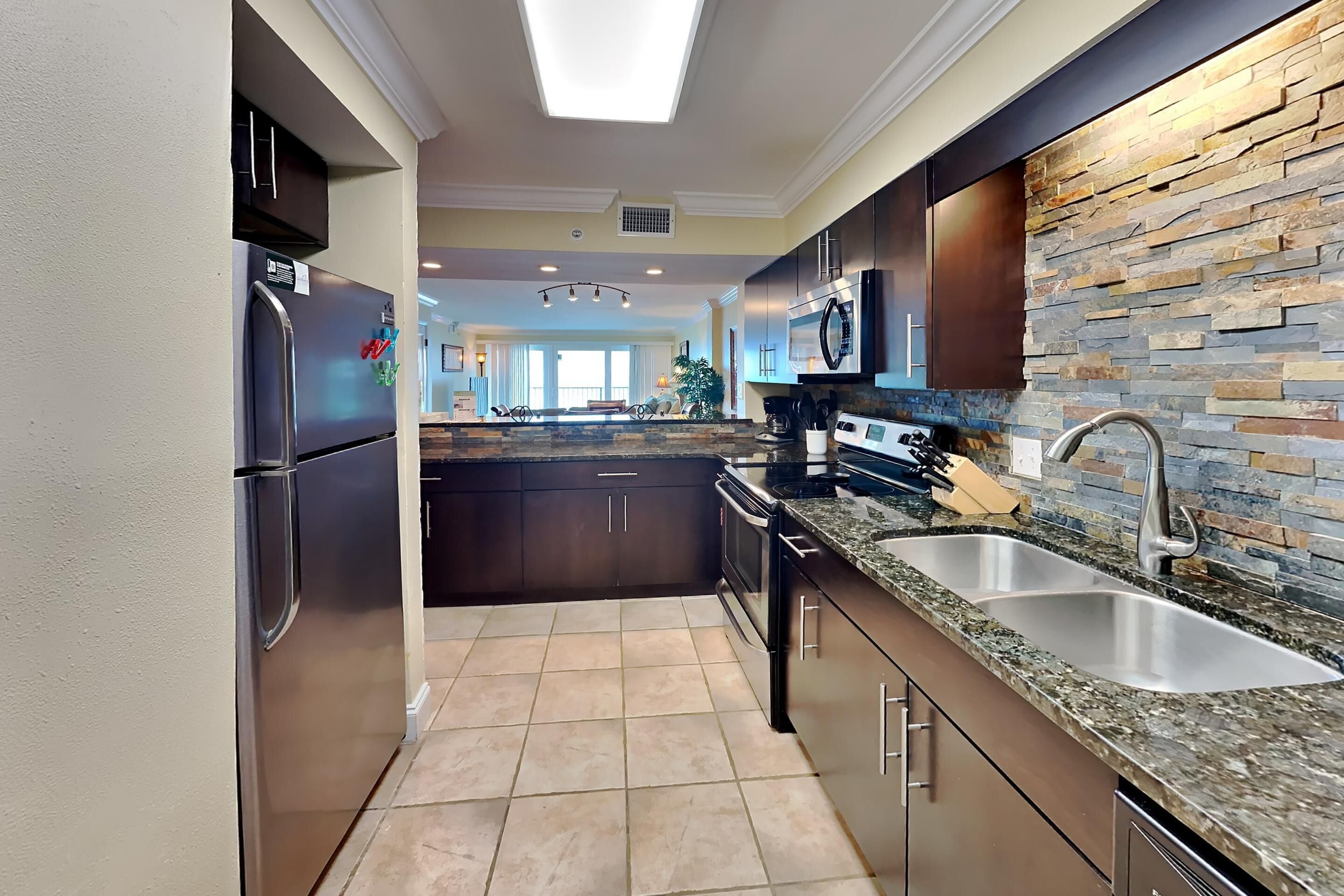 A modern kitchen with stainless steel appliances, a granite countertop, and a stone backsplash.