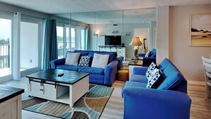 A modern living room with a blue sofa set, a coffee table, and a TV. - Sea Oats by Southern Vacation Rentals (Fort Walton Beach)