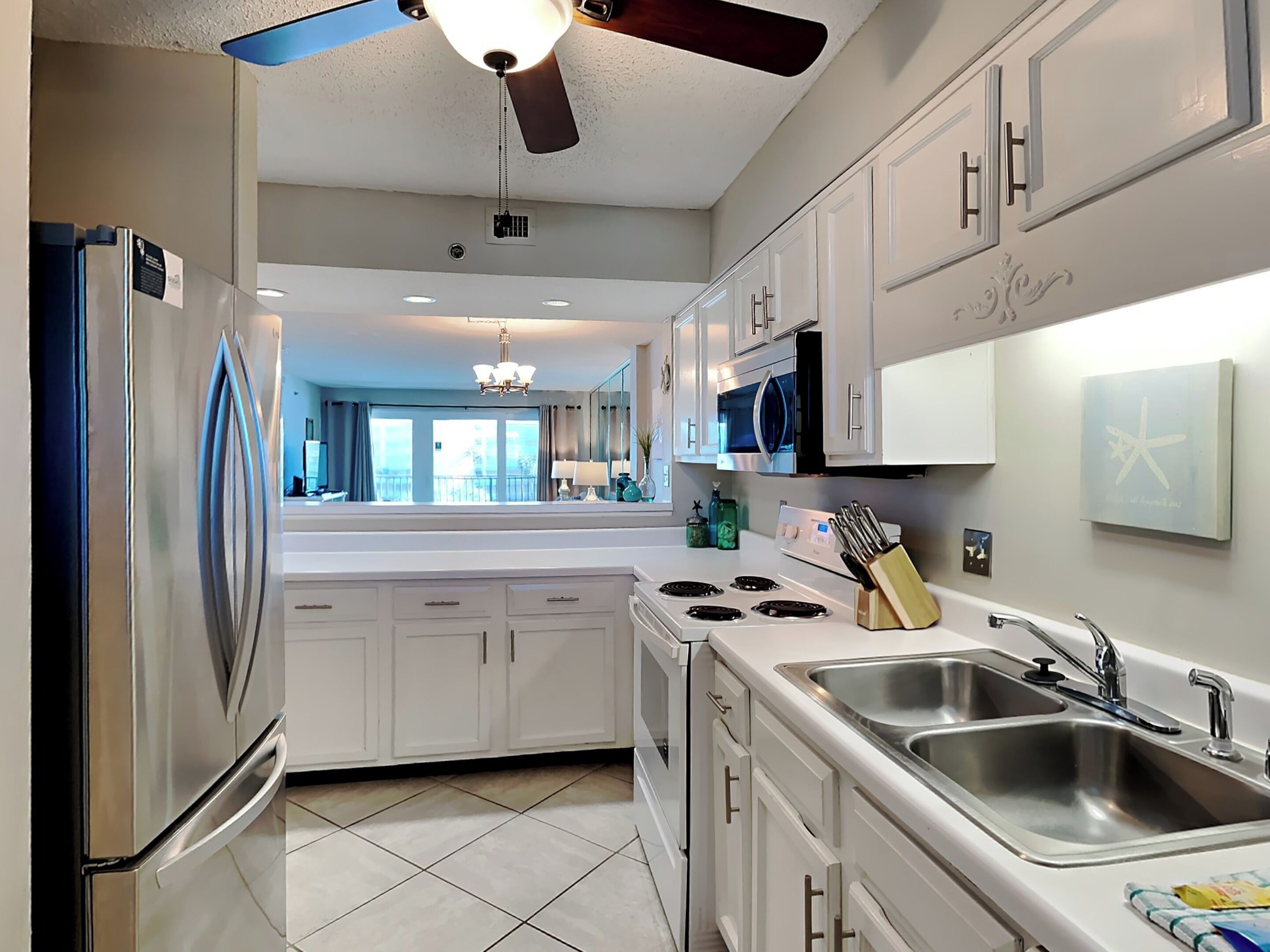A modern kitchen with white cabinets, a stainless steel refrigerator, a gas stove, and a double sink.