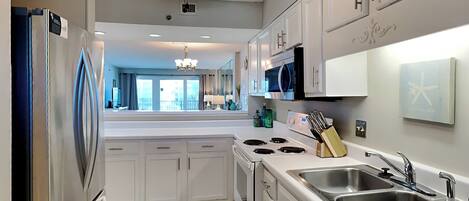 A modern kitchen with white cabinets, a stainless steel refrigerator, a gas stove, and a double sink.