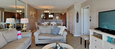 A living room with a sofa, a coffee table, a TV, and a kitchen in the background.
