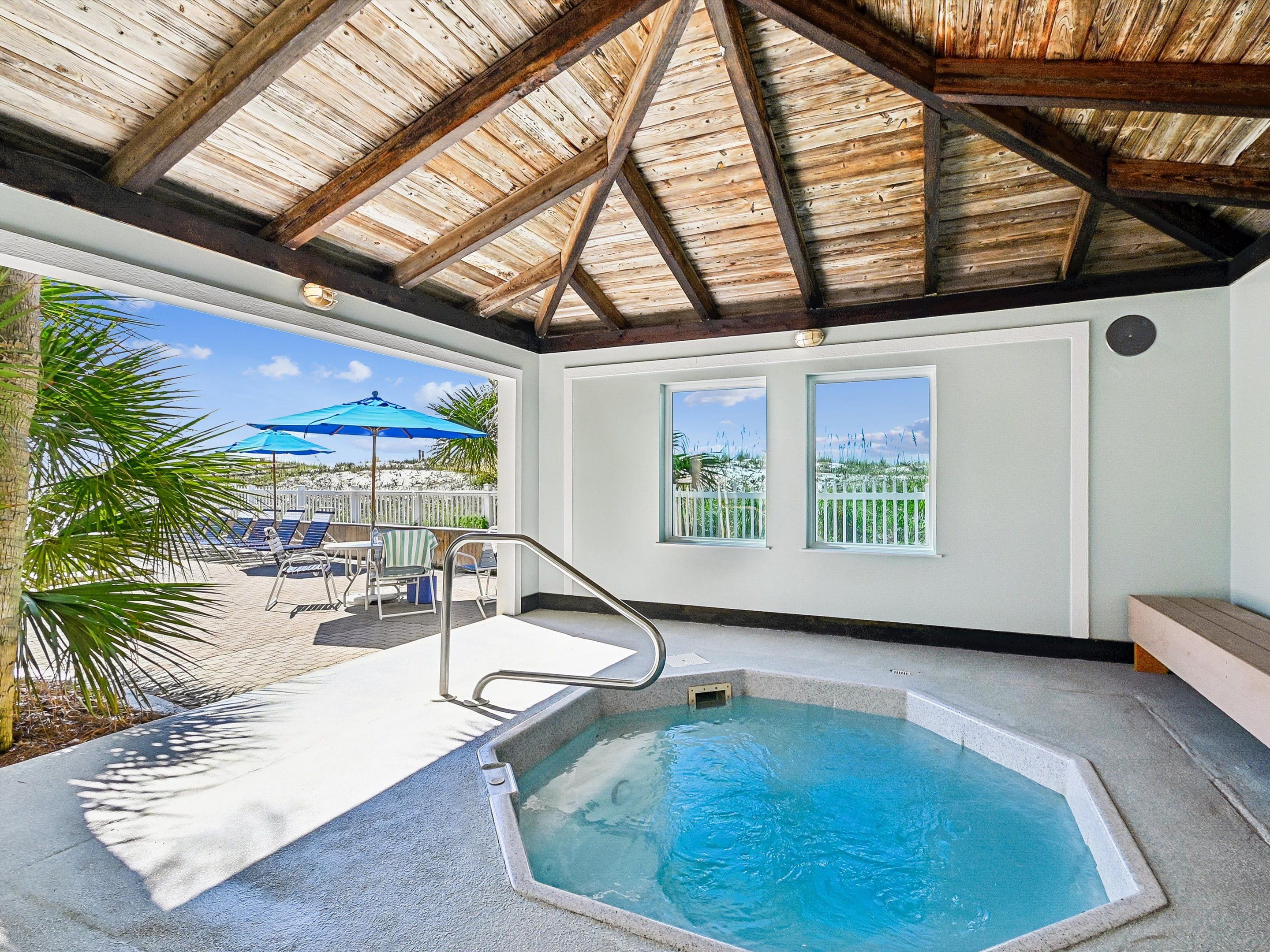 A pool area with a hot tub, a wooden ceiling, and a view of the beach.