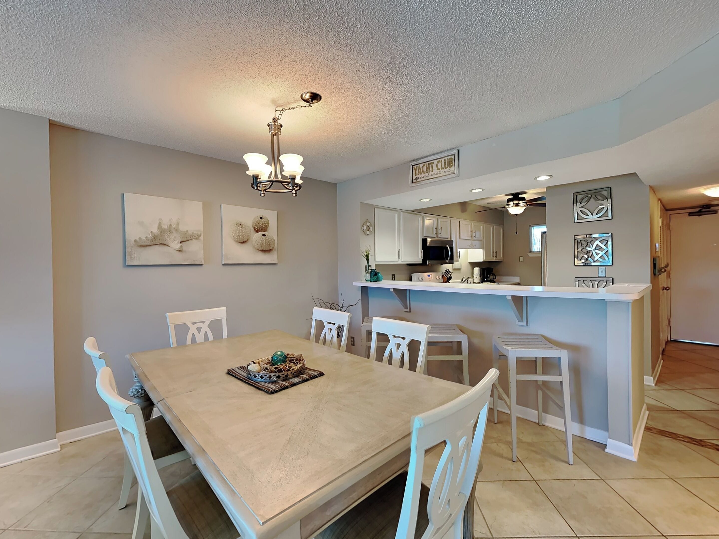 A dining area with a large table and chairs, a kitchen with white cabinets, and a sign that reads "YACHT CLUB".