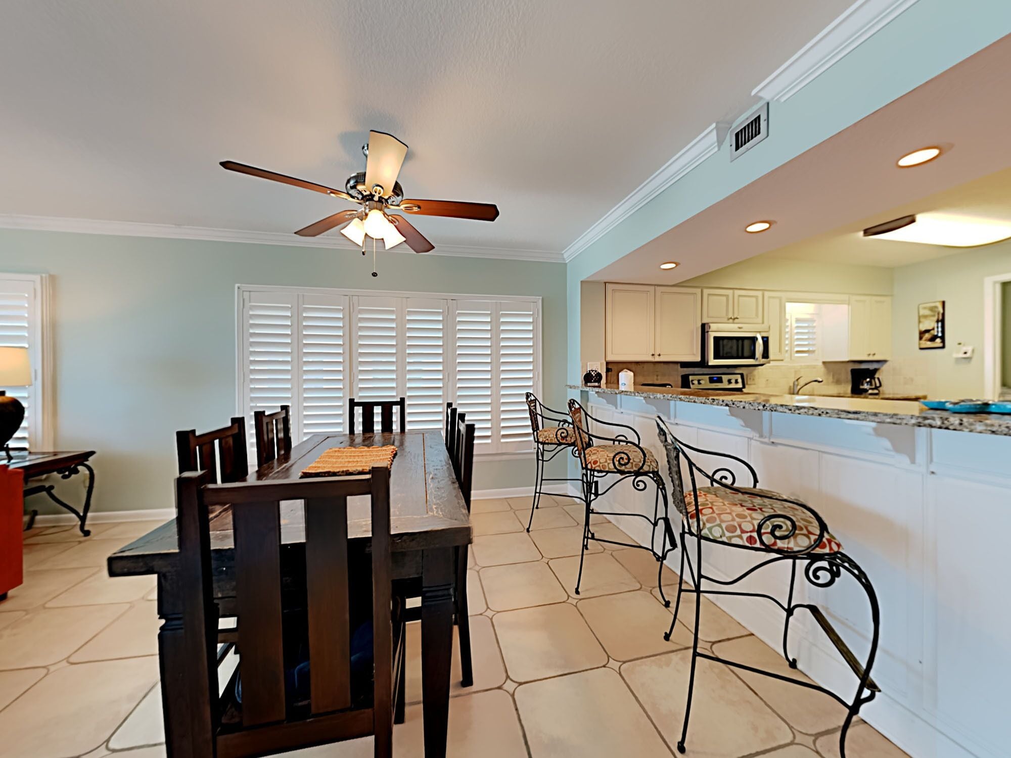 A dining area with a table and chairs, a ceiling fan, and a kitchen with cabinets and appliances.