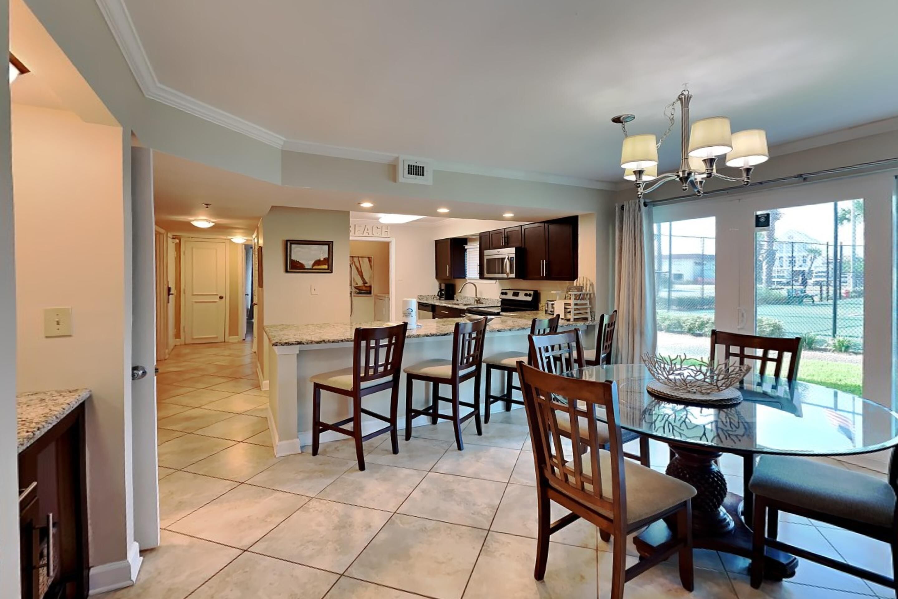 A spacious kitchen with dark cabinets, a central island, and a dining area with a glass table and chairs.
