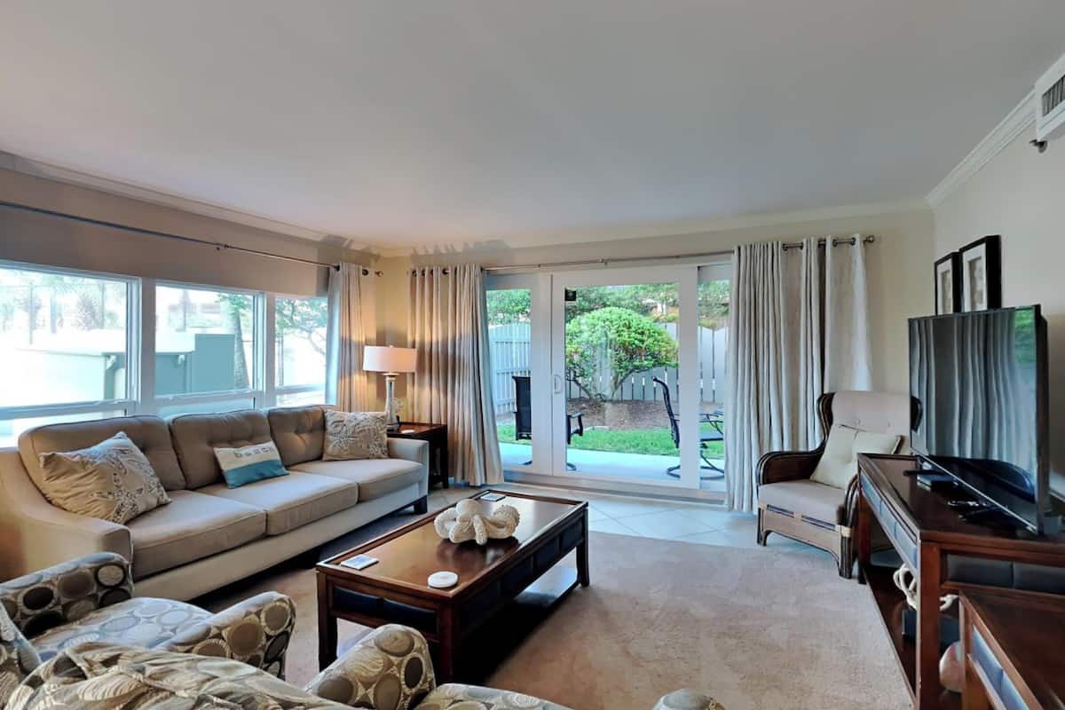 A spacious living room with a sofa, armchairs, a coffee table, and a TV.