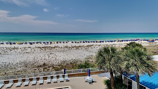 A beach view with a row of sun loungers and umbrellas, a pool area, and a clear blue sky. - Sea Oats by Southern Vacation Rentals (Fort Walton Beach)