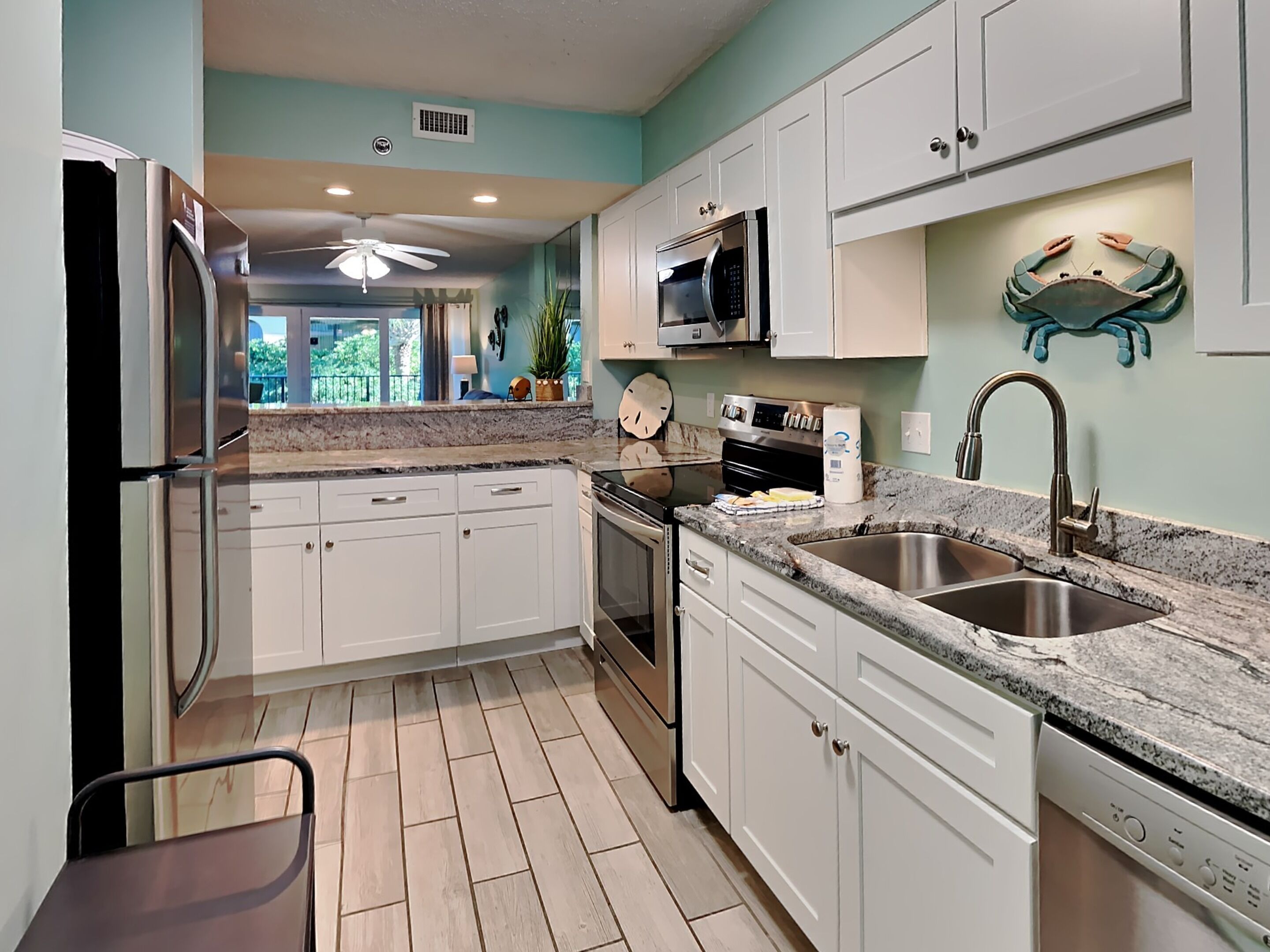 A modern kitchen with white cabinets, a stainless steel sink, a microwave, and a ceiling fan.