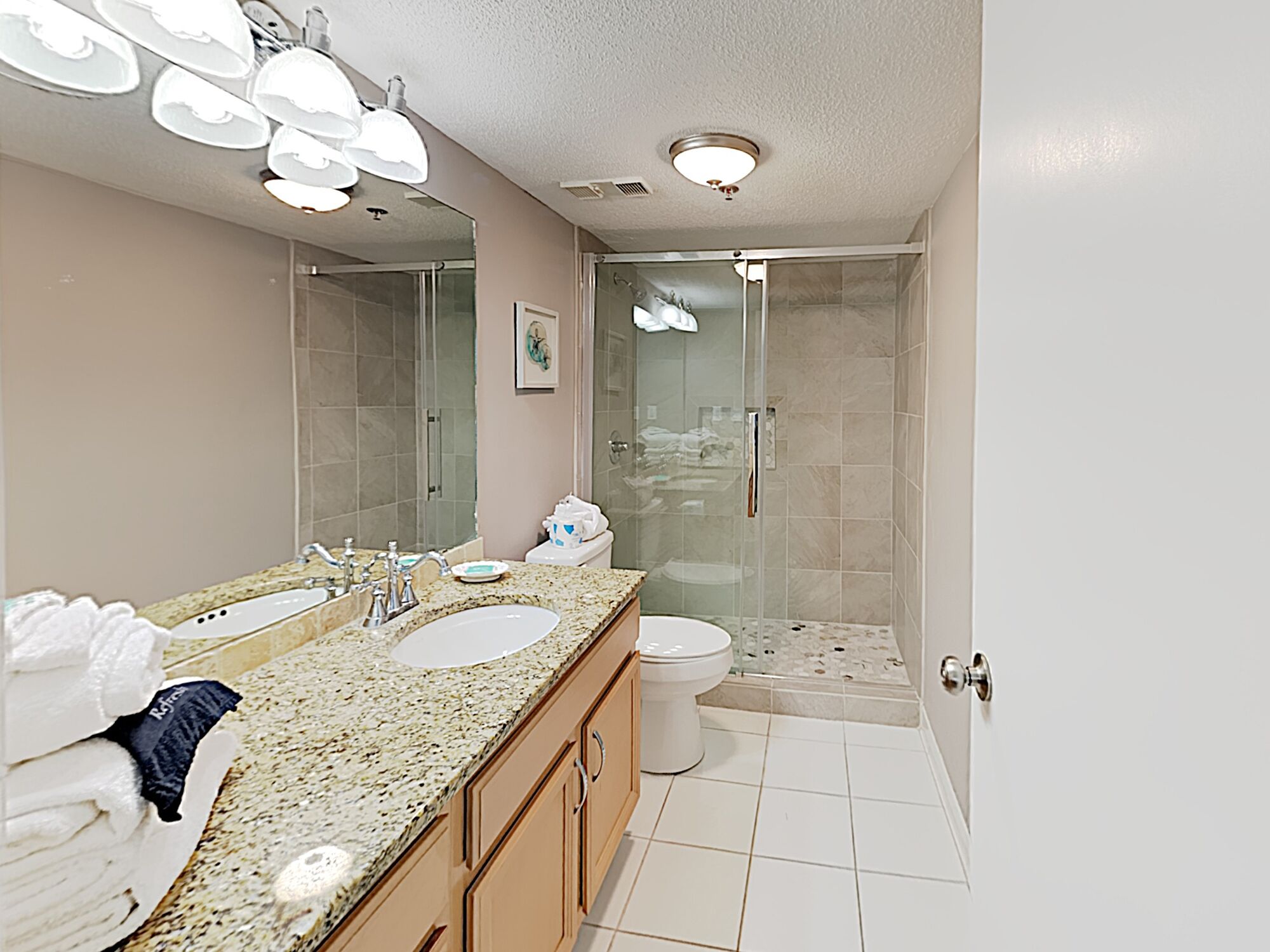 A bathroom with a double sink, a toilet, a shower, and a glass-enclosed shower area.