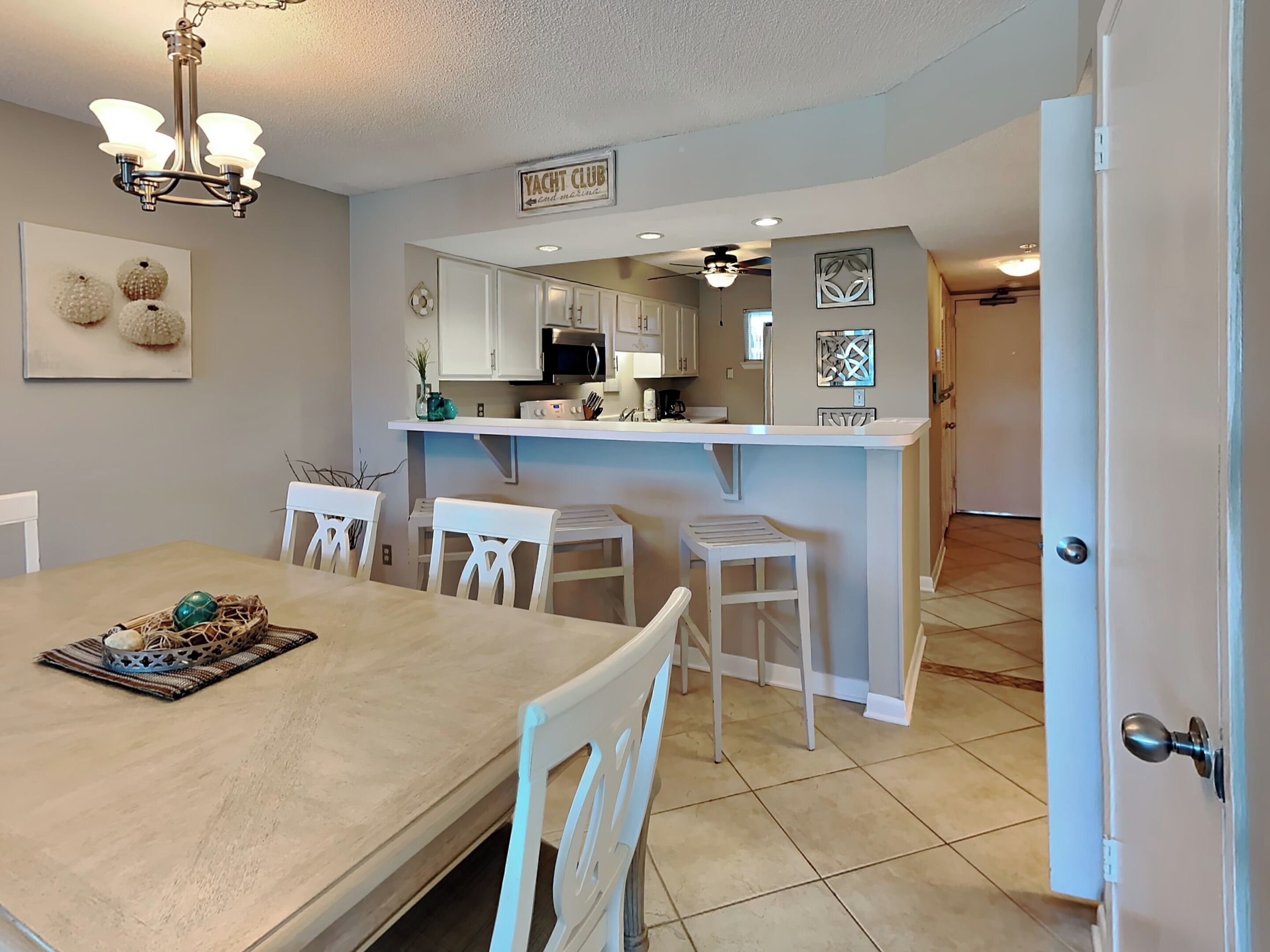 A modern kitchen with white cabinetry, a central island, and a dining area with a wooden table and white chairs.