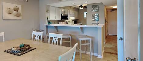 A modern kitchen with white cabinetry, a central island, and a dining area with a wooden table and white chairs.