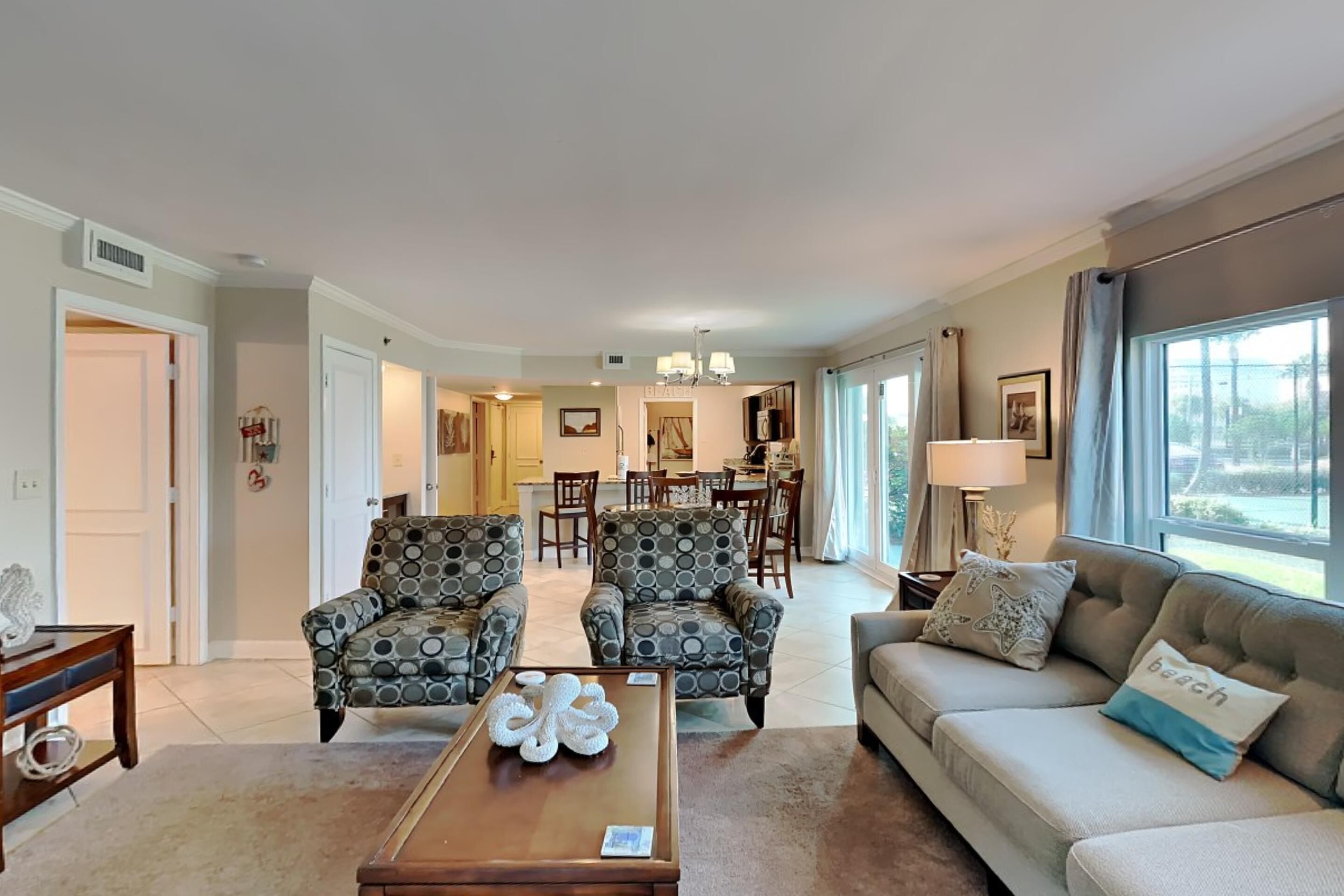 A spacious living room with a sofa, armchairs, and a coffee table. There is a dining area in the background with a table and chairs.