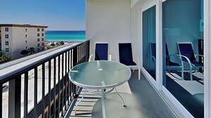 A balcony with a glass table and chairs, overlooking a beach and a hotel building. - Sea Oats by Southern Vacation Rentals (Fort Walton Beach)