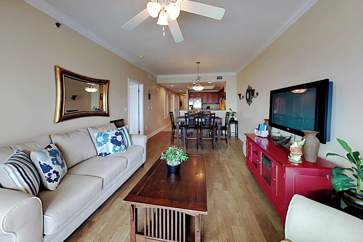 A living room with a sofa, coffee table, TV, and a ceiling fan.