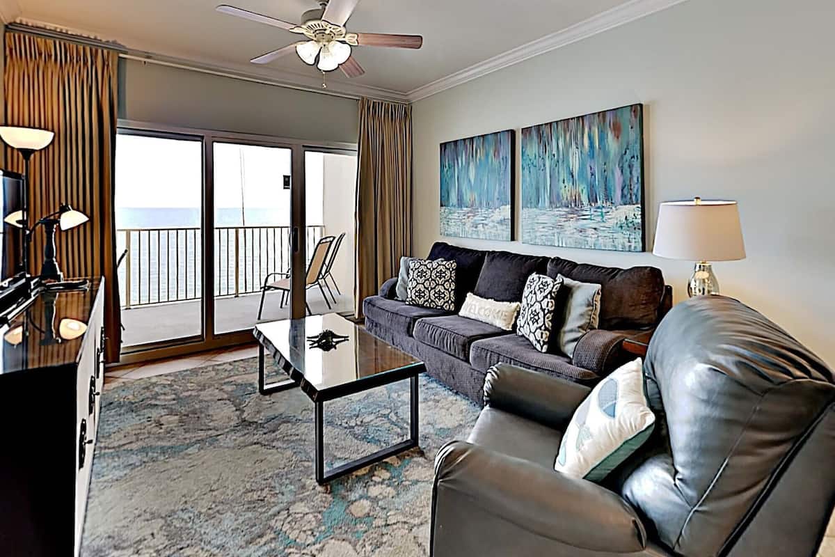 A hotel room with a balcony, a sofa, a coffee table, and a TV.