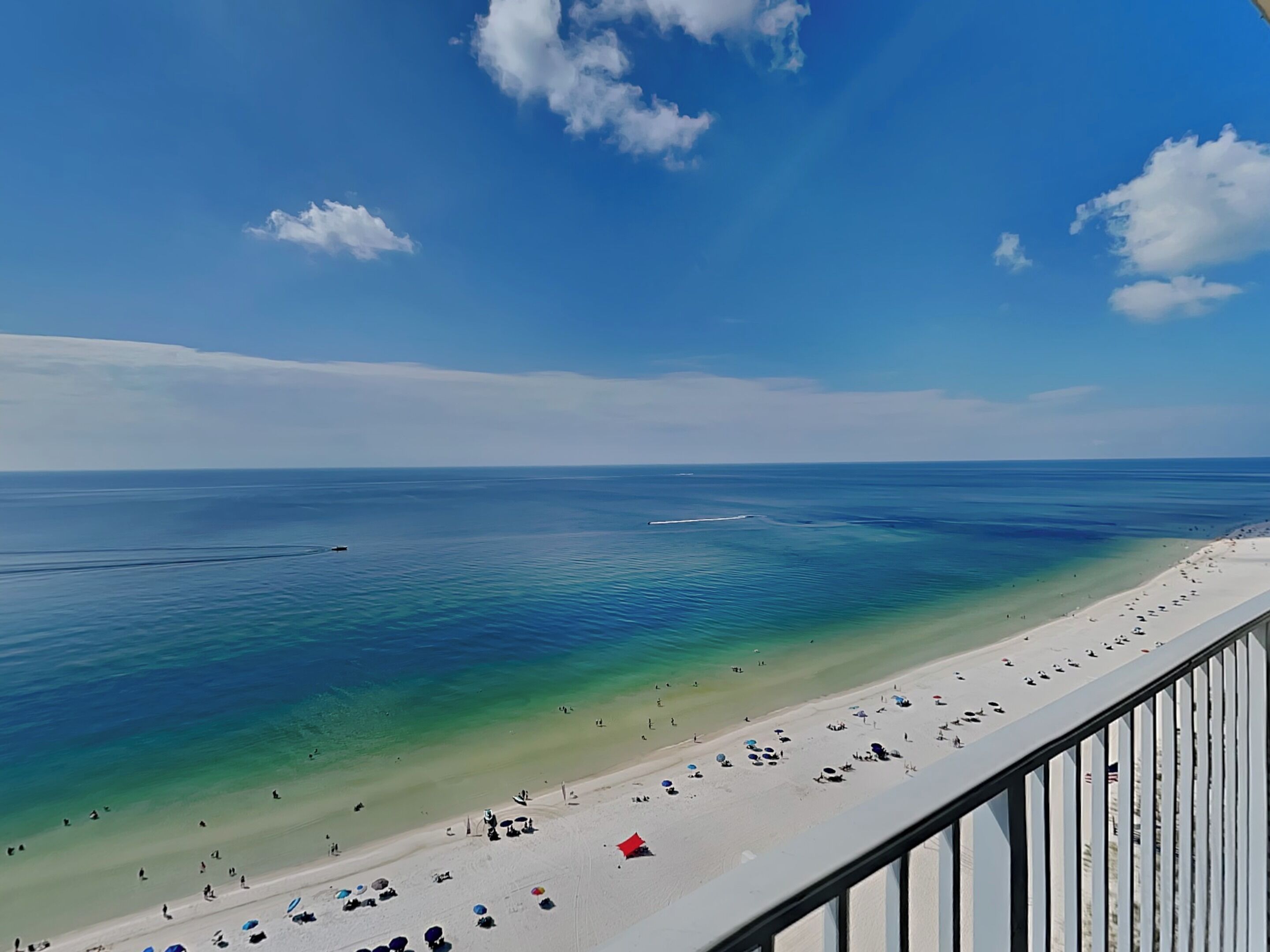 A beach with clear turquoise water, a sandy shore, and a few umbrellas.