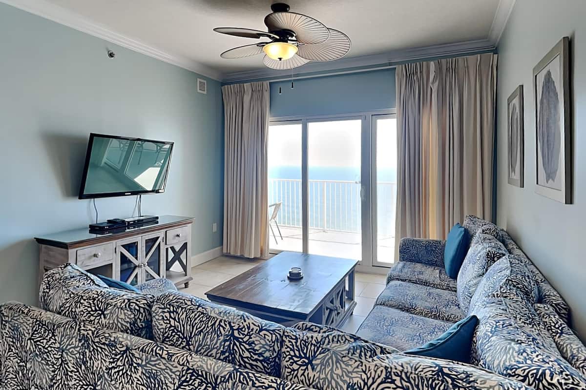 A living room with a sofa, a coffee table, a TV, and a ceiling fan.