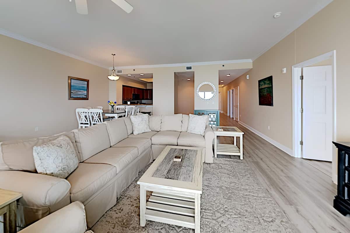 A spacious living room with a large L-shaped sectional sofa, a coffee table, and a dining area with chairs and a table.