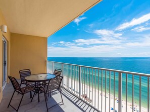 A balcony with a table and chairs, overlooking a beach with clear blue water and a distant shoreline. - Seawind by Southern Vacation Rentals (Gulf Shores)