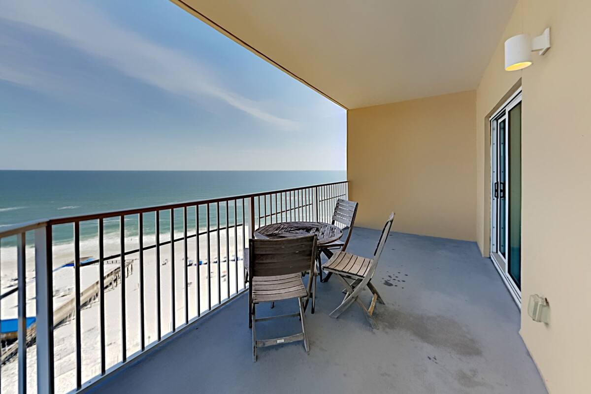 A balcony with a table and chairs, overlooking a beach with a clear view of the ocean.