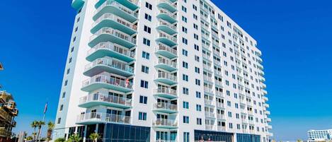 A multi-story hotel with balconies, a pool area, and a beach view.