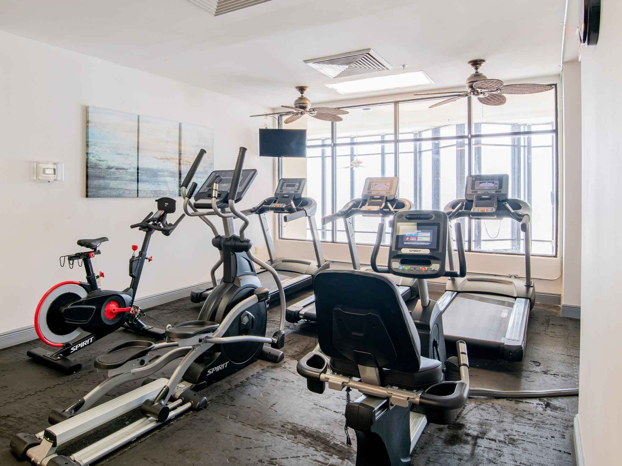 Un gimnasio con diversas máquinas de cardio, una máquina de remo y una cinta de correr.