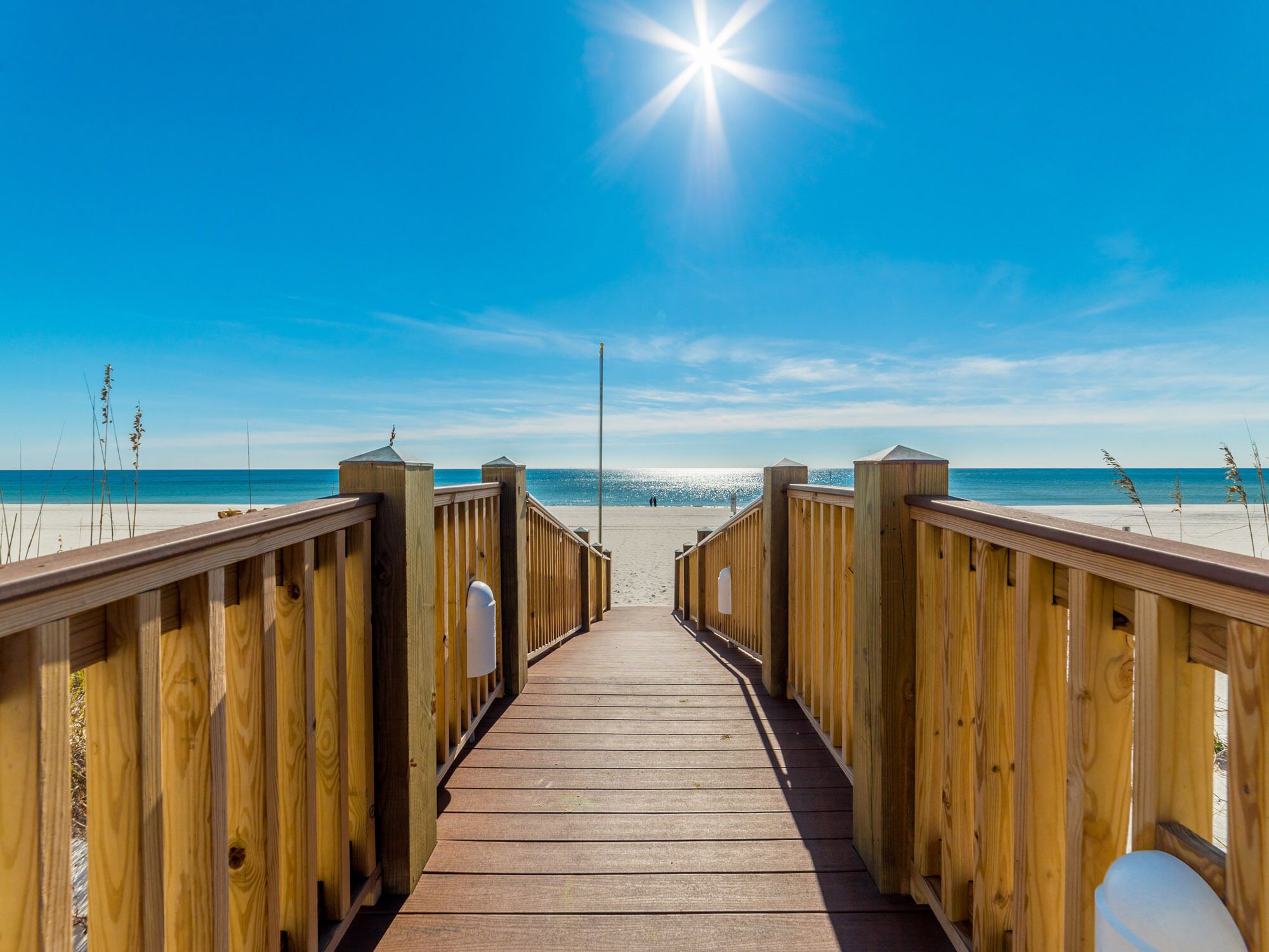 A wooden boardwalk leading to a beach with clear skies and sunlight.