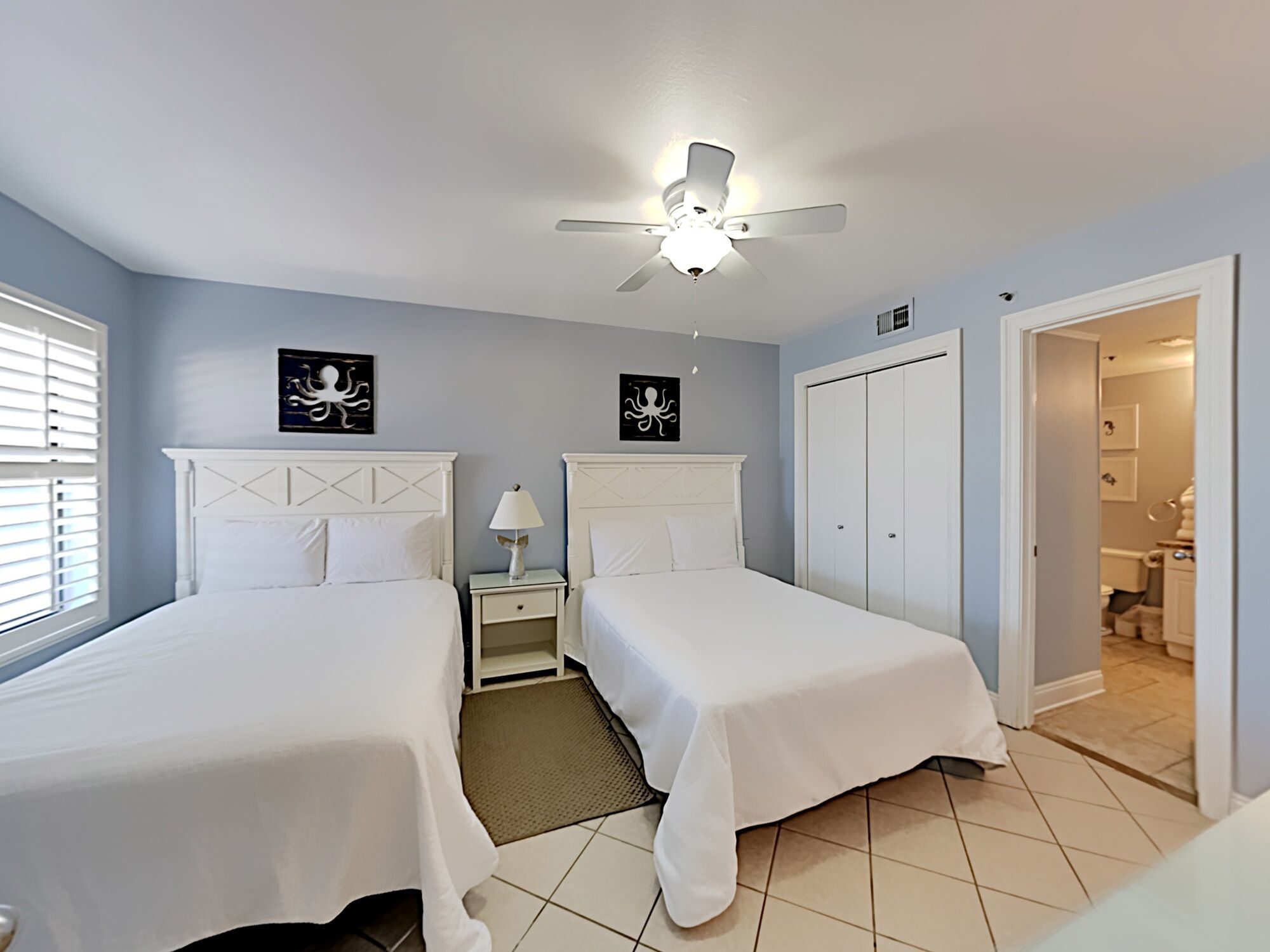 A bedroom with two beds, a ceiling fan, and artwork on the walls.