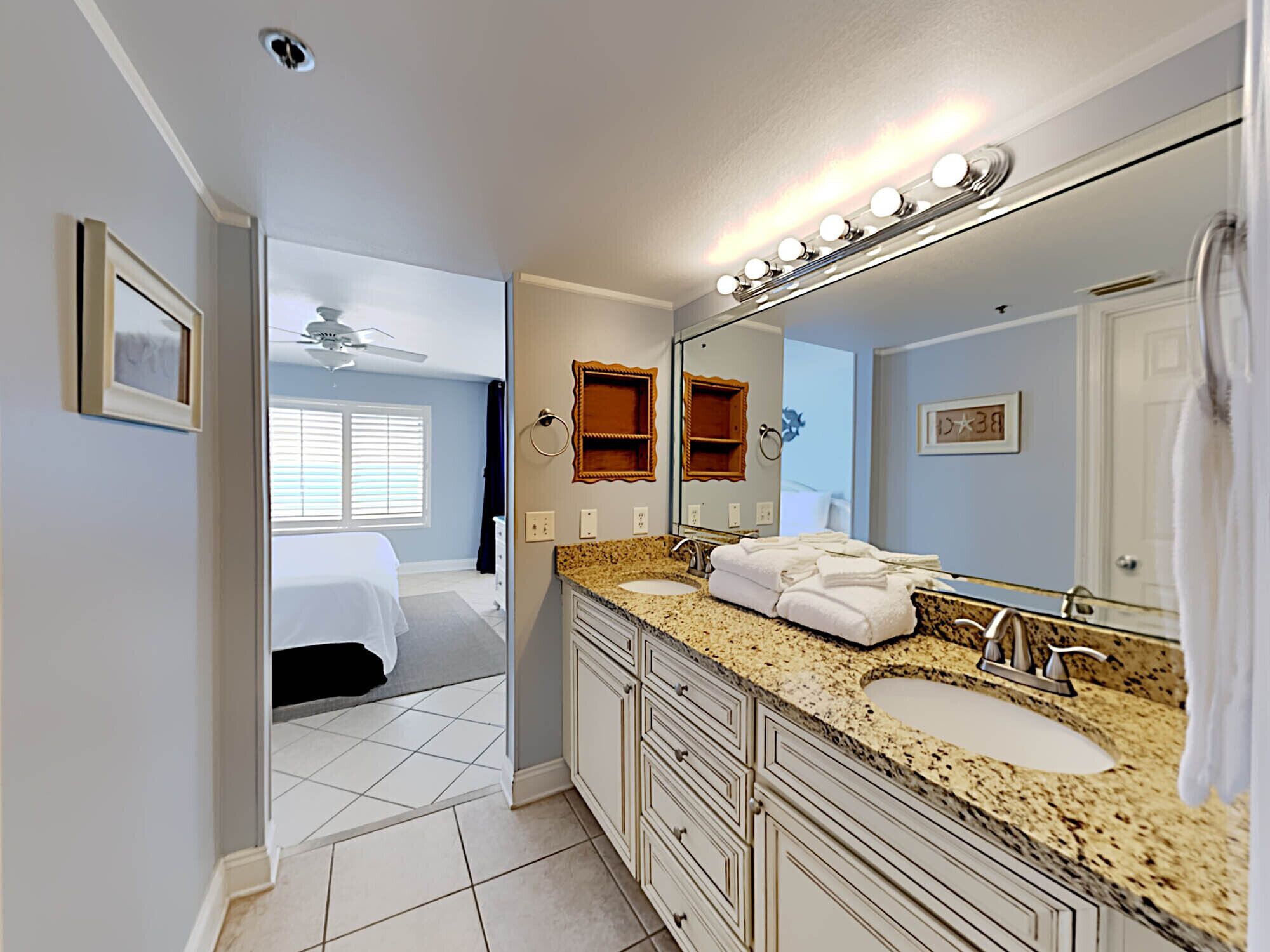 A hotel bathroom with two sinks, a large mirror, and a ceiling fan.