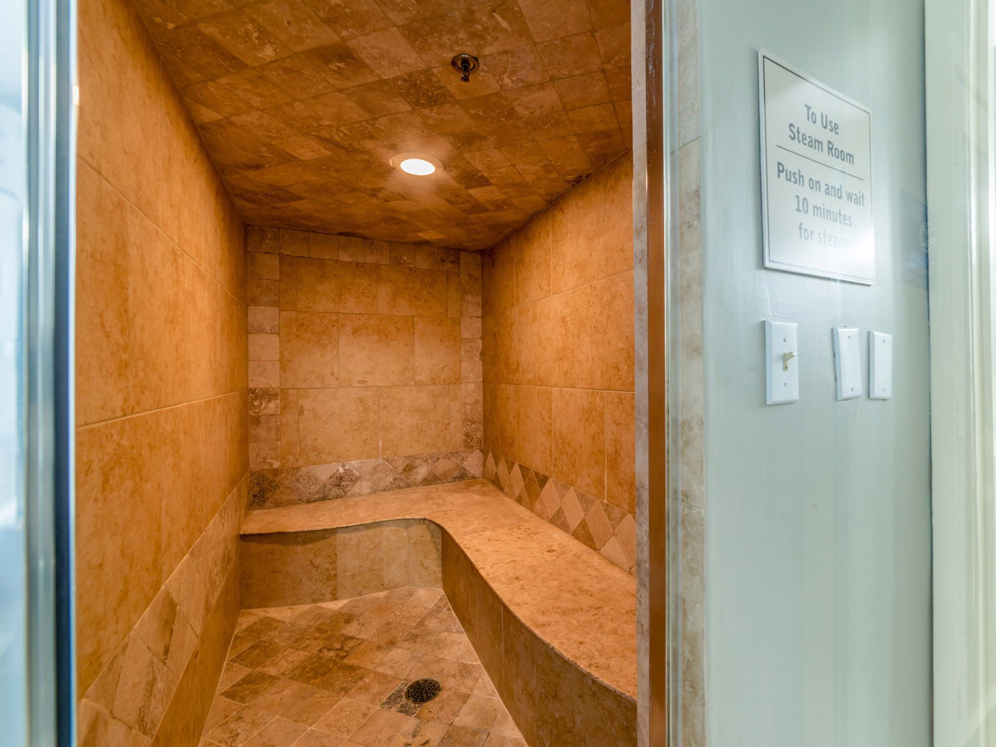 Un baño de vapor con un banco, un cartel en la pared que indica presionar la pared para activar el vapor, y una lámpara en el techo.