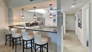 Une cuisine moderne dotée d’un îlot central, de tabourets de bar, de luminaires suspendus et d’un ventilateur de plafond.