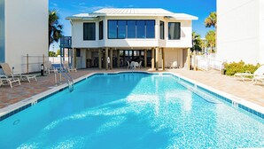Une piscine avec un espace aménagé au bord de l’eau, des chaises longues et un bâtiment à deux étages doté de grandes fenêtres.