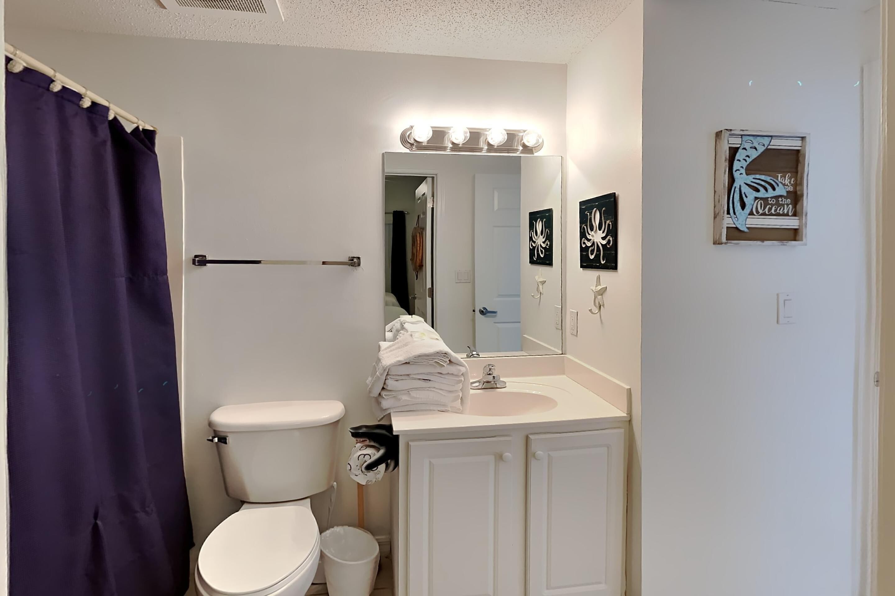 A bathroom with a white toilet, a sink with a mirror above it, and a blue shower curtain.