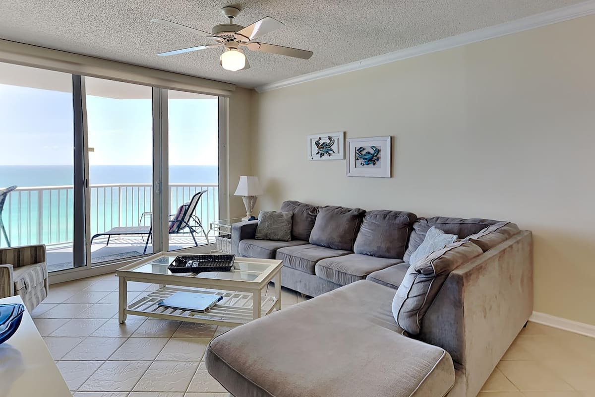 A living room with a sofa, a coffee table, and a ceiling fan. There are two framed pictures on the wall.