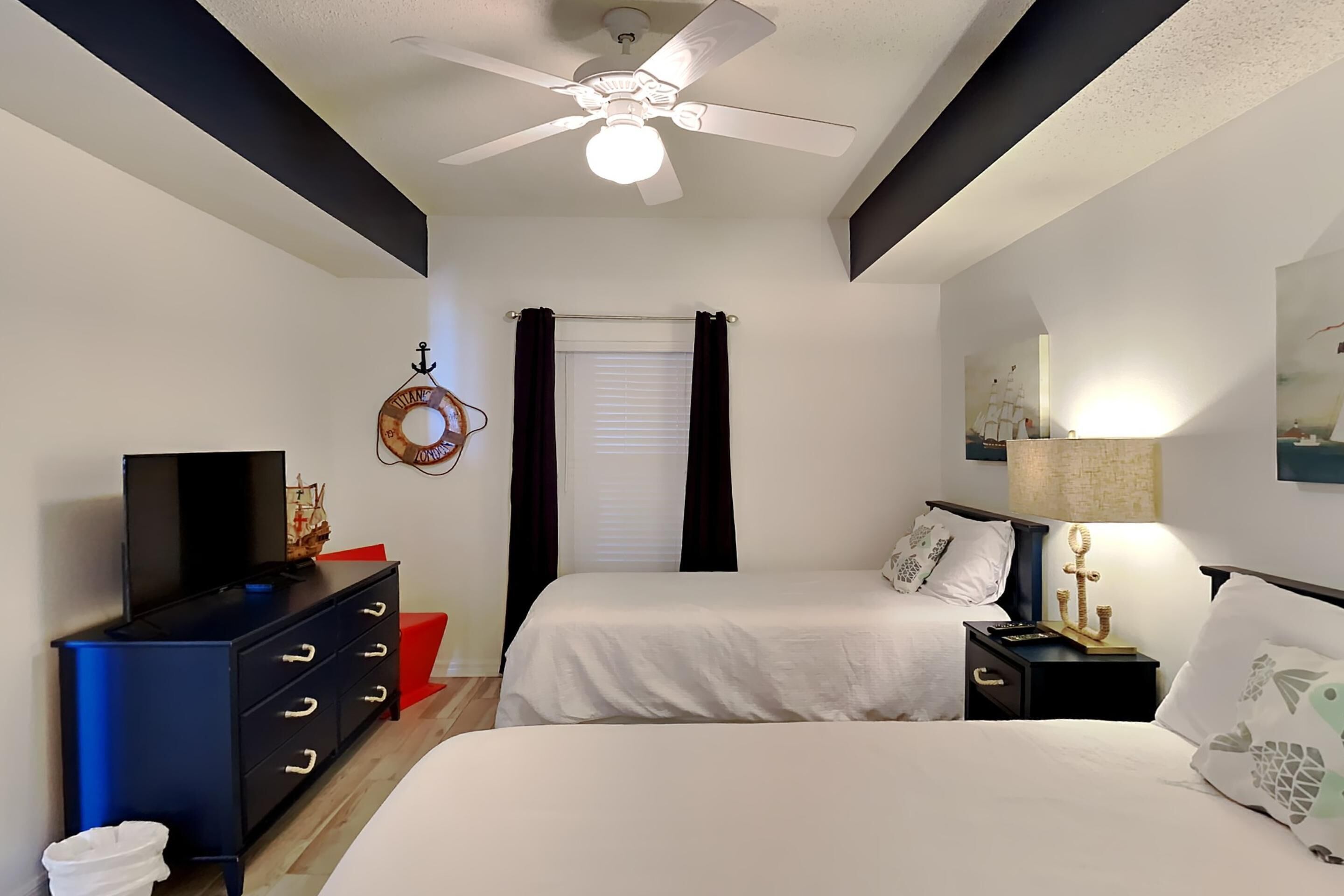 A bedroom with two beds, a ceiling fan, a TV, a dresser, and a nightstand with a lamp.