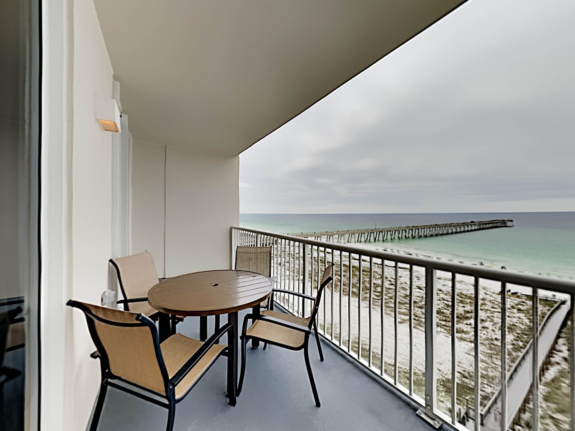 Ein Balkon mit rundem Tisch und Stühlen, mit Blick auf einen Strand und einen Steg.
