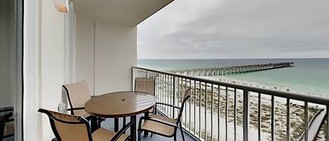 Ein Balkon mit rundem Tisch und Stühlen, mit Blick auf einen Strand und einen Steg.