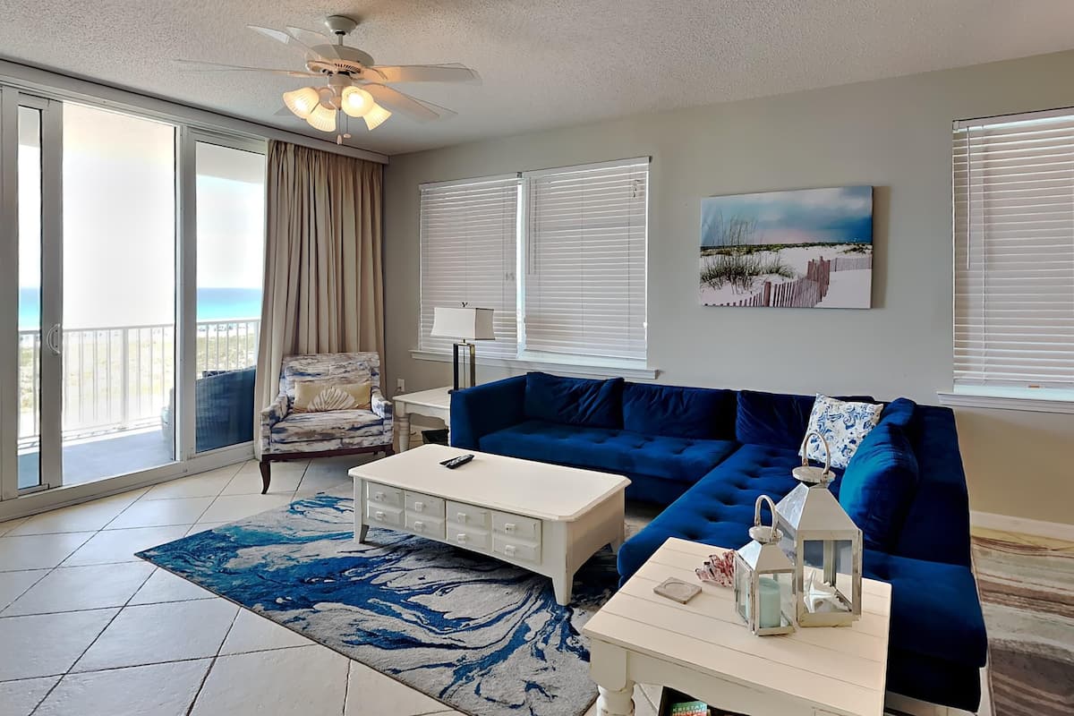 A living room with a blue sofa, a white coffee table, and a view of the ocean through large windows.