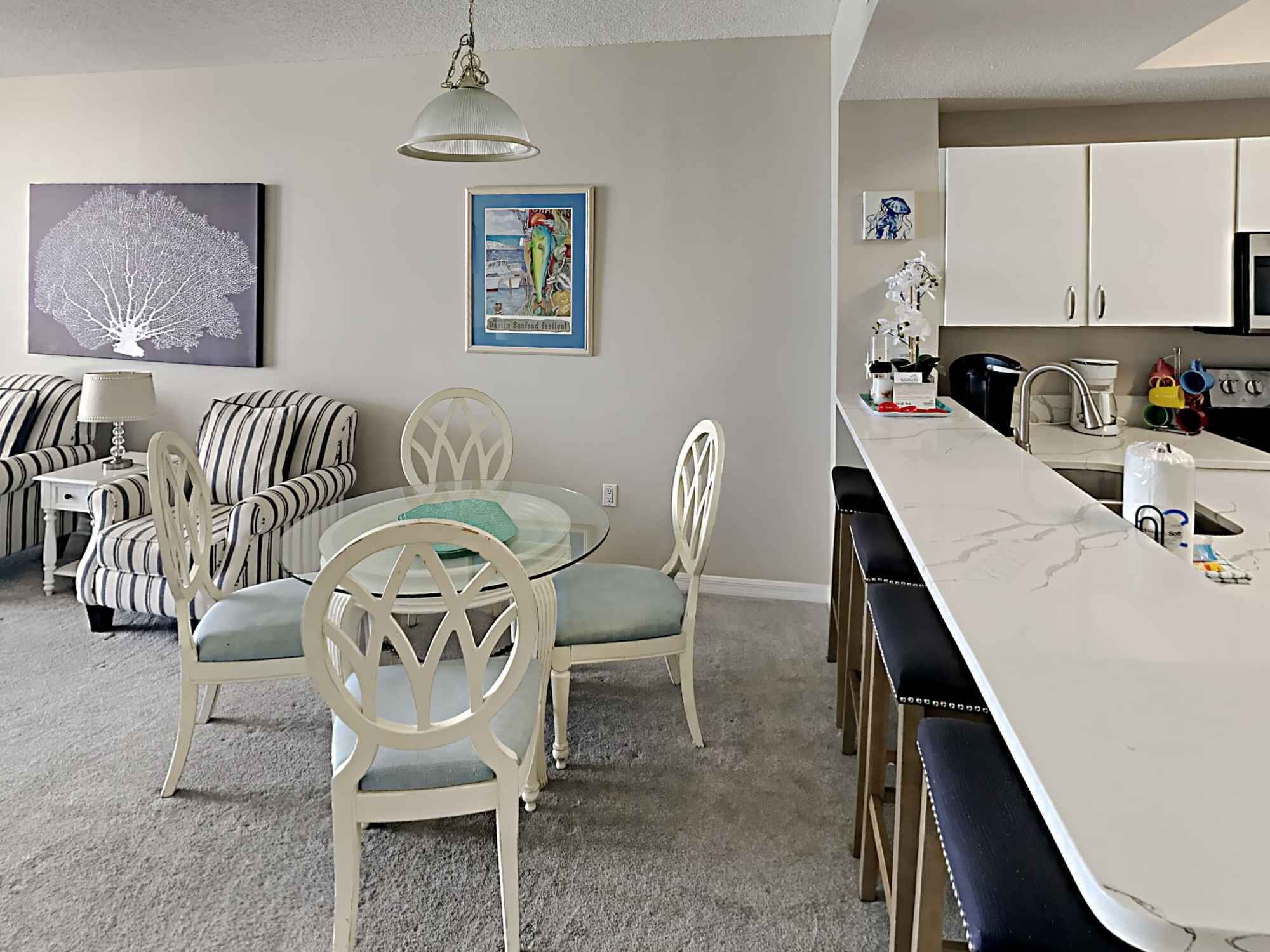 A modern kitchen with white cabinets, a marble countertop, and a dining area with striped chairs and a glass table.